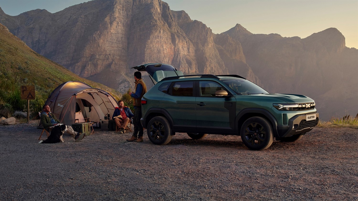 Dacia Duster temno zelene barve, parkiran ob šotoru v gorskem okolju, oseba stoji ob odprtih zadnjih vratih vozila.
