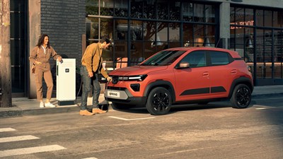 Dacia Spring vozilo oranžno polnjenje na cesti z osebama v mestu