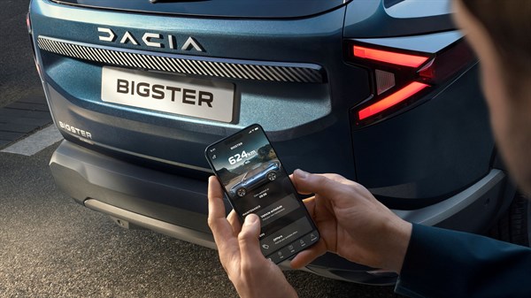 Dacia Bigster vozilo sivo - zadnji del z logotipom in pametnim telefonom v roki.