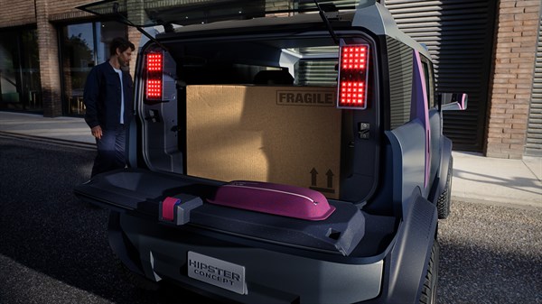 Moški stoji ob strani Dacia Hipster, v prtljažniku je velik kartonski zaboj z napisom "fragile".