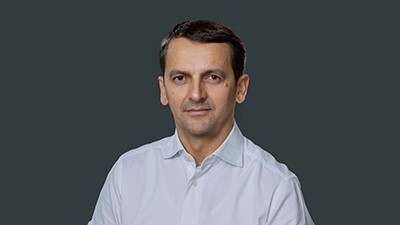 Portret moškega s kratkimi črnimi lasmi v svetli srajci pred temnim ozadjem.