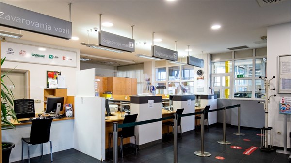 Notranjost poslovnih prostorov z več pulti za zavarovanja vozil.
