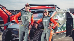 Dva člana ekipe v dirkaških kombinezonih stojita pred dirkalnikom Dacia.