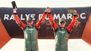 Dirkača v dirkaški opravi pred vozilom Dacia.