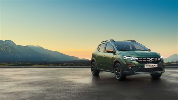 Na sliki je nova Dacia Sandero Stepway v zeleni barvi, postavljena pred čudovito gorsko kuliso ob sončnem zahodu.