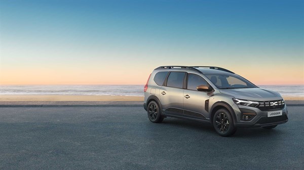 Na sliki je Dacia Jogger, parkirana ob morju med sončnim vzhodom ali zahodom. Vozilo je prikazano v elegantni sivi barvi, z modernim in prostornim dizajnom.