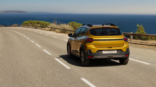 Rumeni Dacia Sandero Stepway od zadaj bočno na cestni ovinku ob morju.