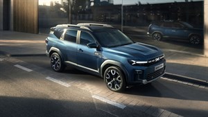 Dacia Bigster modro sprednji tričetrtinski pogled na mestnem parkirišču ob stekleni fasadi