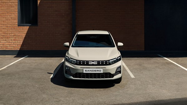 Beli Dacia Sandero sprednji pogled na parkirišču ob zidani stavbi.