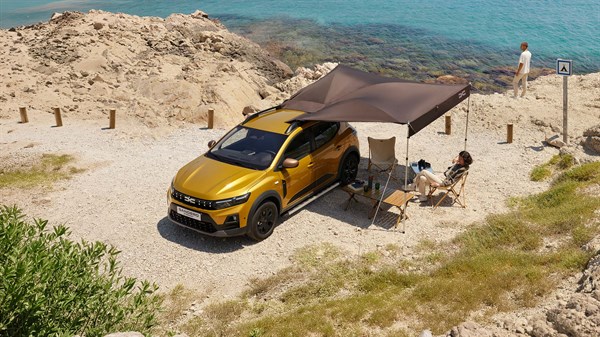 Dacia Stepway, rumene barve na skalnati obali z razpeto strešno tendo, dve osebi sedita ob vozilu.