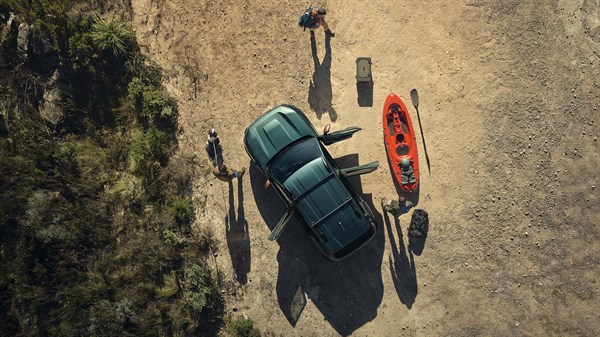 Dacia Duster temno zelene barve, pogled od zgoraj, parkiran na peščenih tleh ob rdečem kajaku, ob vozilu stojita dve osebi.