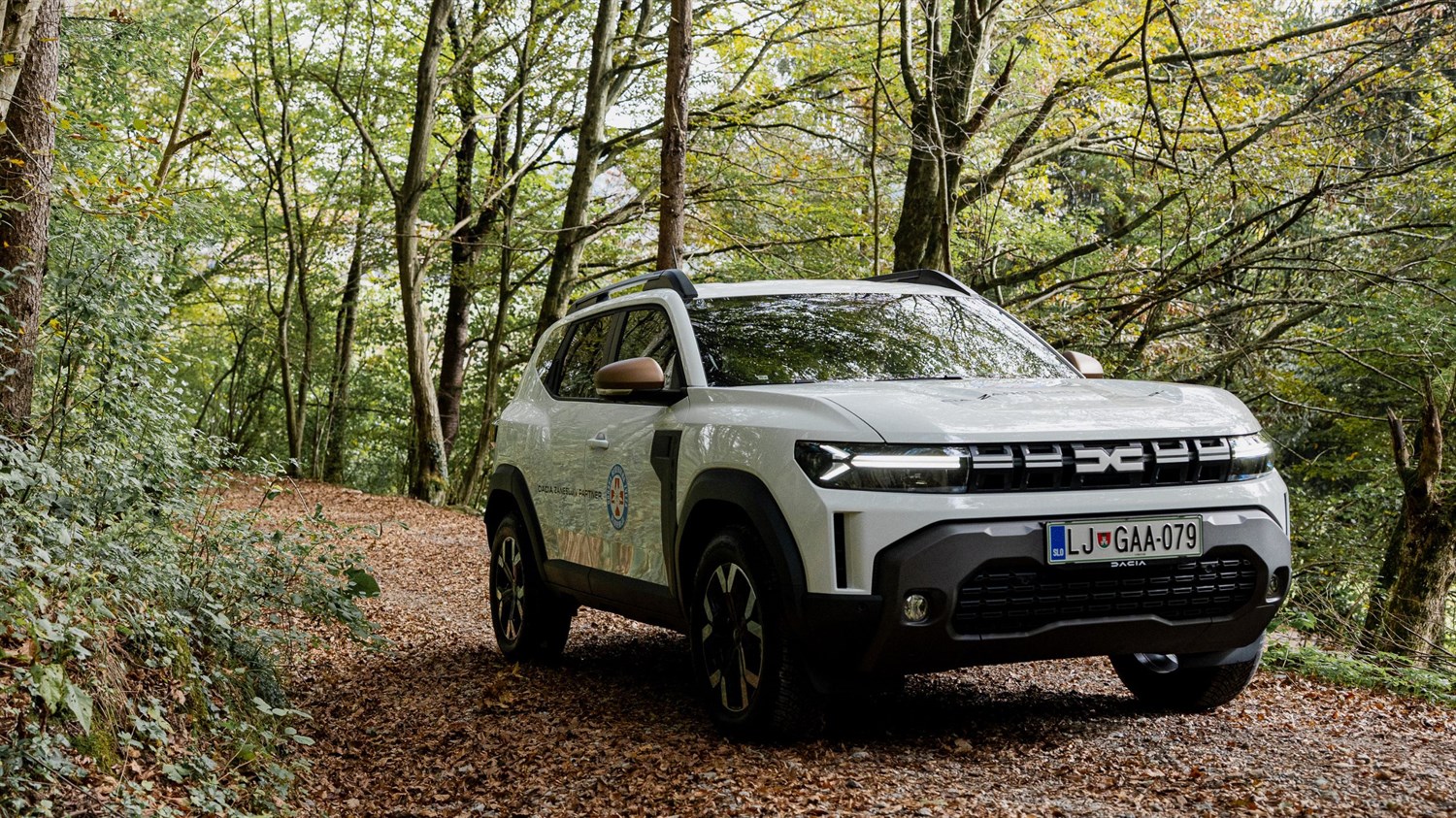 Beli Dacia Duster, med vožnjo po podeželski cesti; na vratih napis "DACIA. ZANESLJIV PARTNER." in okrogel logotip GRS.