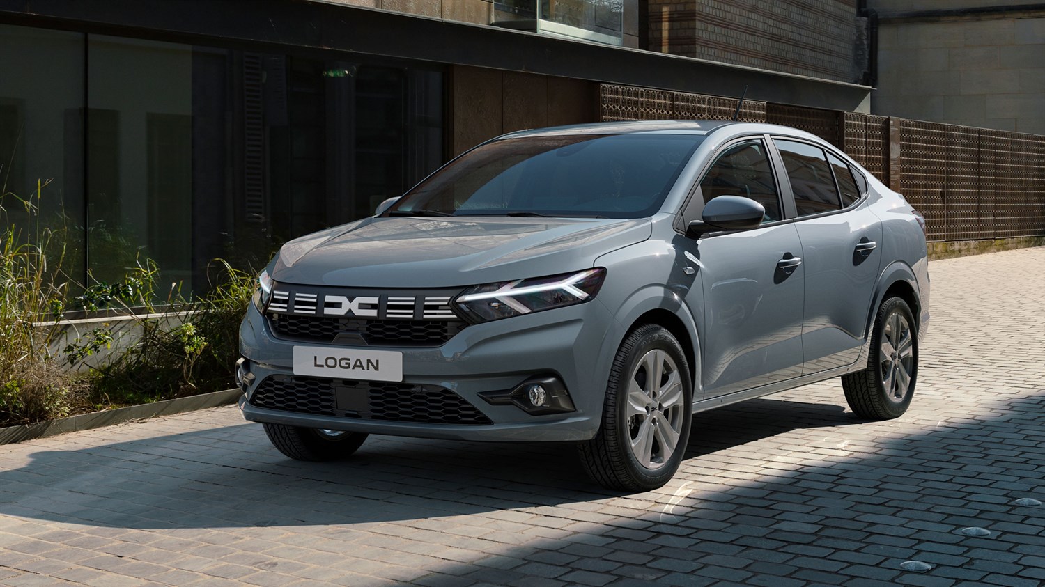 Dacia Logan siva barva, sprednji bočni pogled pred stavbo na tlakovani ulici