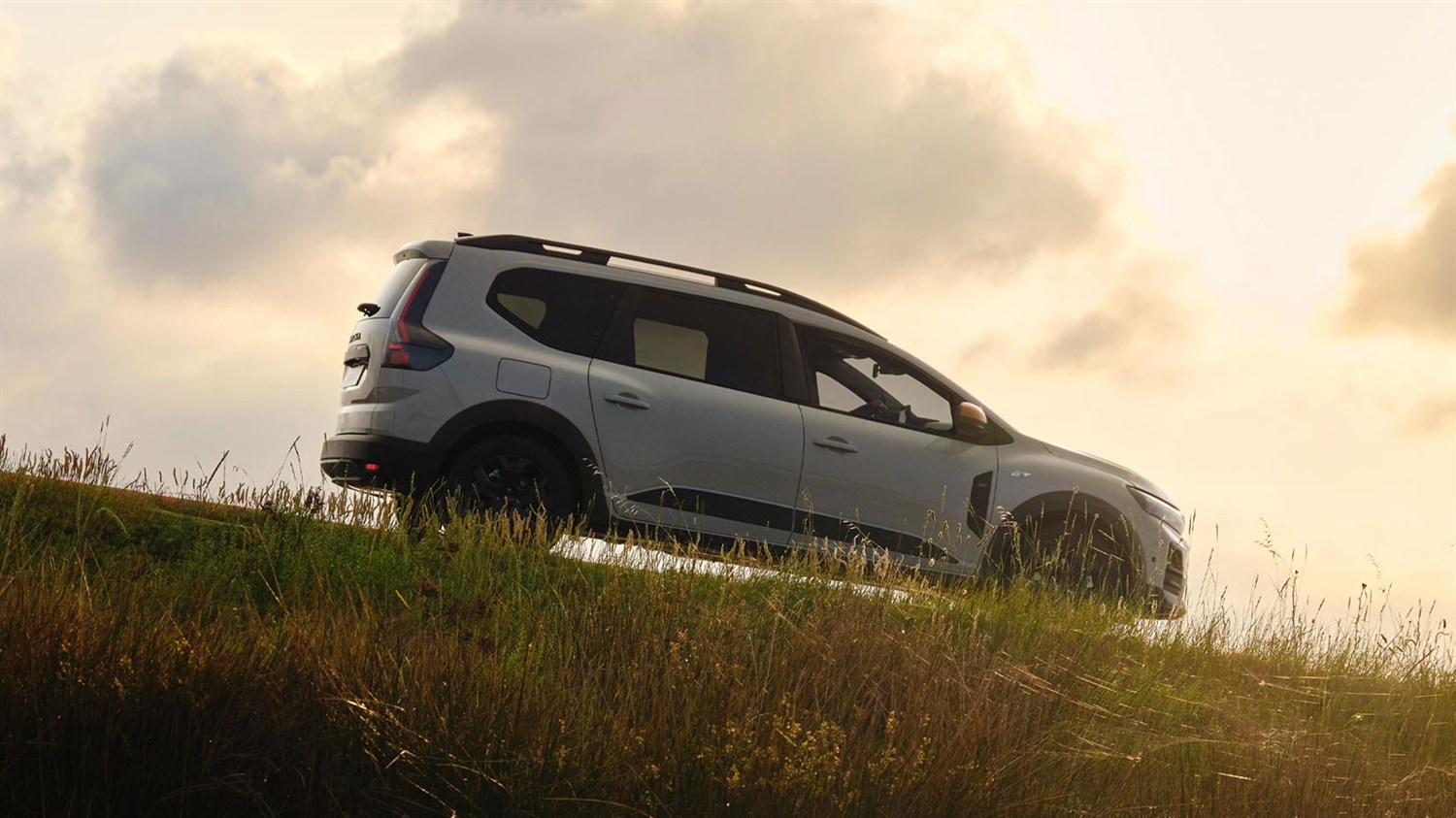 Beli Dacia Jogger bočni profil na travniku pri sončnem zahodu
