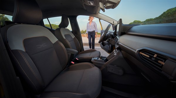 Notranjost vozila Dacia z sprednjima sedežema in žensko ob odprtih vratih.