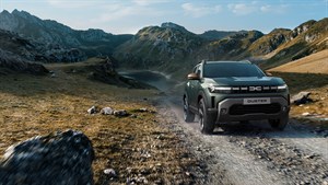 Sivi Dacia Duster vozi po makadamski poti v goratem okolju.