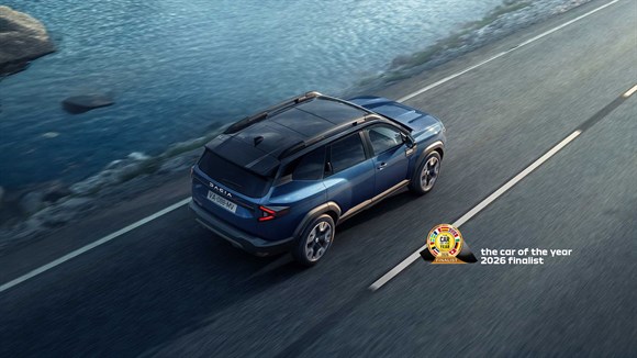 Modri Dacia Bigster vozi po cesti ob vodi, pogled od zgoraj.