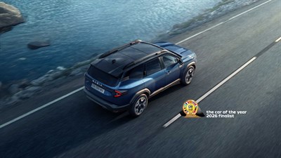 Temno modri Dacia Bigster, med vožnjo po mostu ob vodi; v levem spodnjem kotu znak “the car of the year 2026 finalist”.