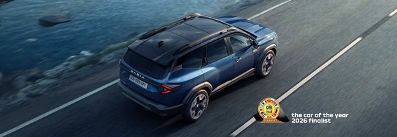 Modri Dacia Bigster med vožnjo po cesti ob obali, pogled od zadaj zgoraj.