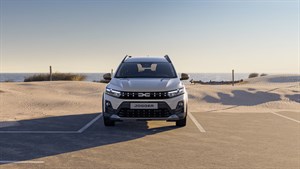 Na sliki je svetel Dacia Jogger, prikazan v prednjem pogledu, parkiran ali ustavljen na parkirišću z nežnim naravnim ozadjem.