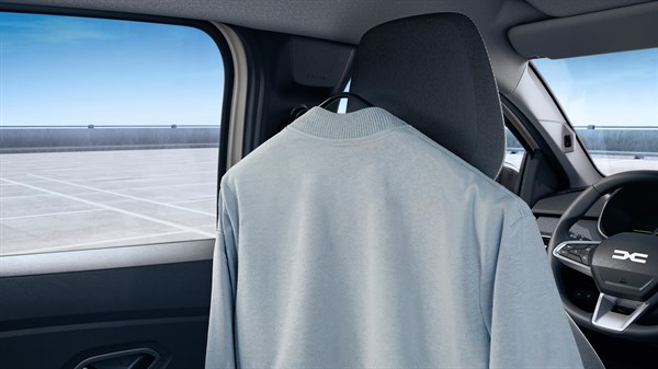 Na sliki je notranjost vozila, posneta iz zadnjega dela kabine. Na vzglavniku sprednjega sedeža visi svetel kos oblačila, zataknjen na kljukico za obešanje.