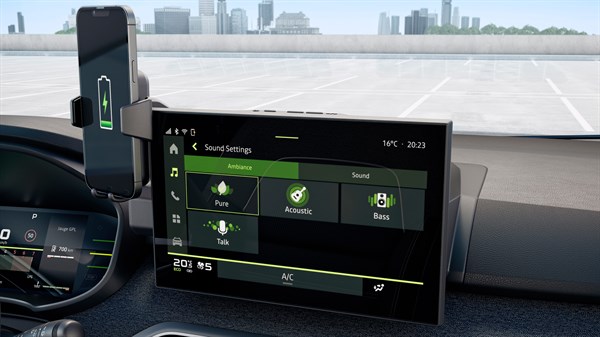 Na sliki je notranjost vozila s poudarkom na osrednjem multimedijskem zaslonu. Prikazan je meni nastavitev zvoka z možnostmi, kot so Pure, Acoustic, Bass in Talk, razdeljenimi v kategorijo Ambiance. Na vrhu zaslona sta prikazana ura in temperatura. Levo od multimedijskega zaslona je nameščen pametni telefon v nosilcu, na katerem je prikazan simbol baterije.