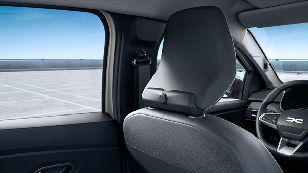 Na sliki je notranjost vozila, posneta iz zadnjega sedeža. V ospredju je naslonjalo sprednjega sedeža z vzglavnikom v temno sivi tkanini.