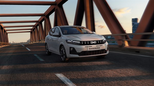 Beli Dacia Sandero, ki vozi po mostu v času sončnega zahoda.