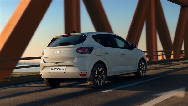 Na sliki je bel mestni avtomobil Sandero s petimi vrati, prikazan z zadnje strani. Parkiran je na praznem, označenem parkirišču.