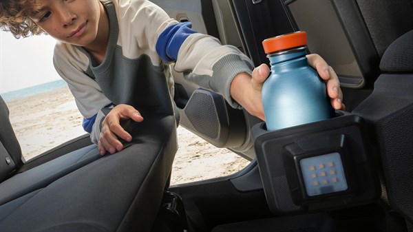 Na sliki otrok iz zadnjega sedeža seže po aluminijasti steklenički, ki je odložena v modularni YouClip nosilec, pritrjen na zadnji del sredinske konzole.