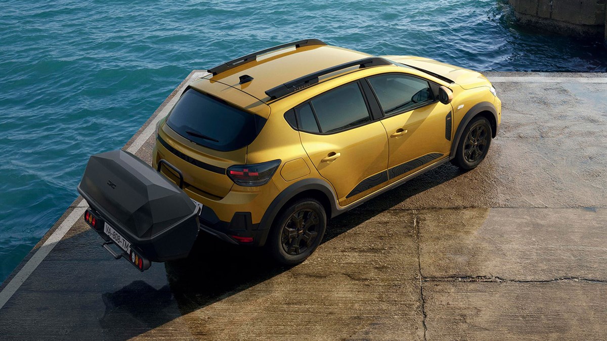 Rumeni Dacia Sandero Stepway, zadnji pogled s prtljažnikom na vlečni kljuki ob vodi.