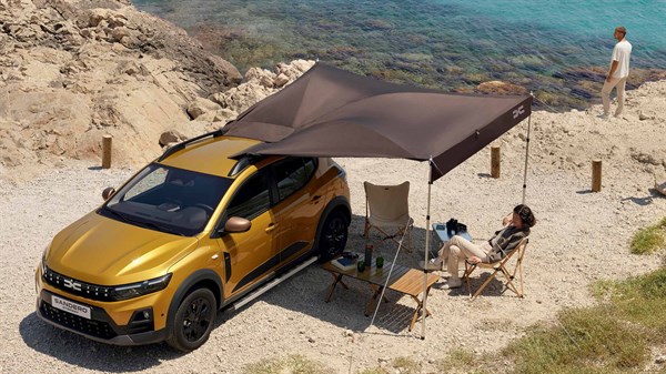 Rumeni Dacia Sandero Stepway s šotorom in osebami na plaži.