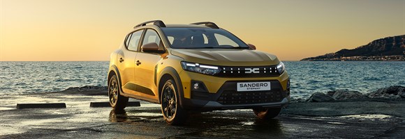 Na sliki je rumen Dacia Sandero Stepway, parkiran ob morski obali ob sončnem zahodu.