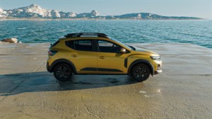 Slika prikazuje vozilo Sandero Stepway v zlato-rumeni barvi z boka parkirano ob morju.