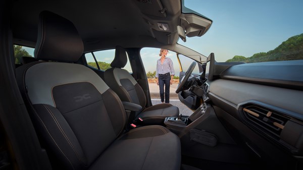 Na sliki je notranjost vozila, posneta iz perspektive sovoznikovega sedeža proti odprtim vratom na voznikovi strani.