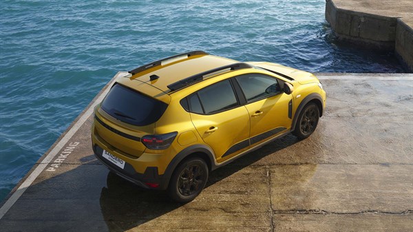 Na sliki je rumeni Dacia Sandero Stepway, parkiran ob morski obali ob sončnem zahodu, prikazano z zadnje strani.