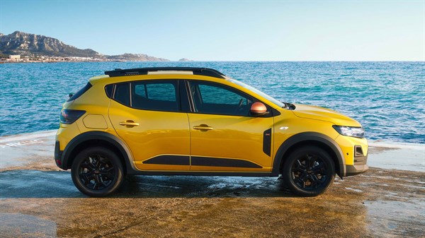 Na sliki je rumeni Dacia Sandero Stepway, parkiran ob morski obali ob sončnem zahodu, prikazano opazovalcu z bočne strani.