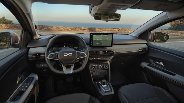 Na sliki je notranjost vozila Dacia Sandero Stepway, posneta s perspektive potnika na zadnjih sedežih. Prikazan je celoten prednji del kabine.