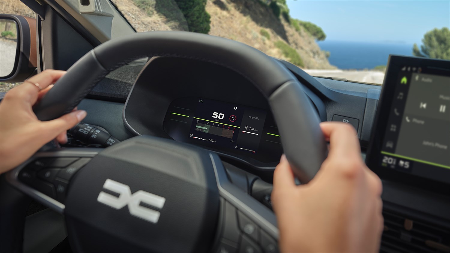 Slika prikazuje insturmentalno ploščo za volanskim obročom na katerem je viden emblem znamke Dacia.