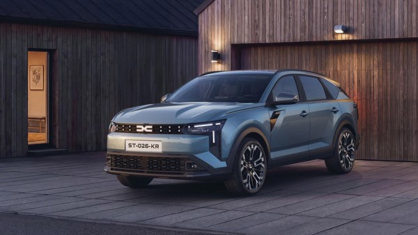 Dacia Striker svetlo modre barve, sprednji bočni pogled pred leseno hišo v večernem vzdušju.