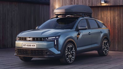 Dacia Striker svetlo modre barve s strešnim kovčkom pred leseno hišo.