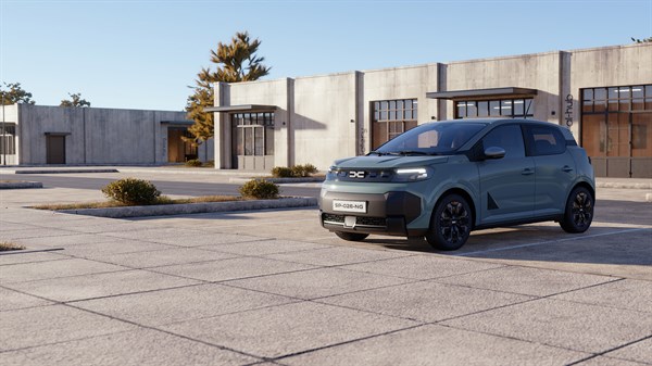 Dacia Spring v svetlo zeleni barvi, parkiran pred sodobno industrijsko stavbo