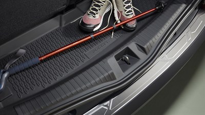 Prtljažni prostor vozila Dacia Jogger s plastično zaščito, pohodniškimi čevlji in zložljivo palico za hojo.